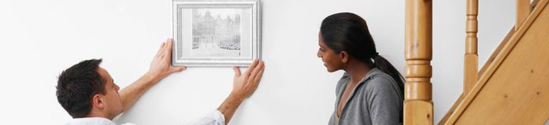 Man leveling a picture frame while a woman inspects