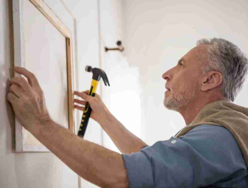 Man holding a hammer positioning a picture frame on a wall to be level