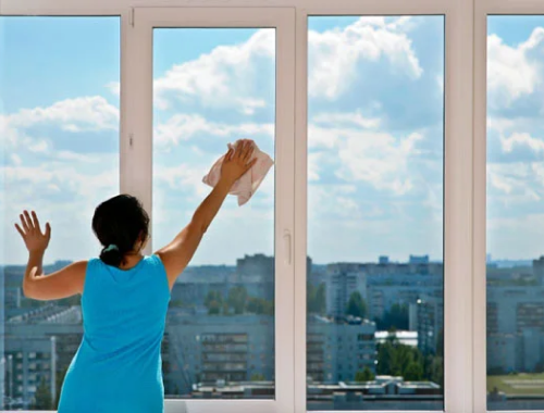 Woman cleaning large windows from inside the building